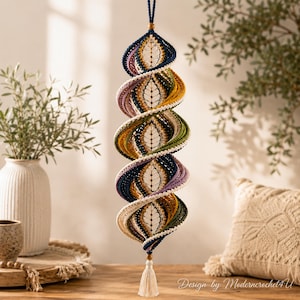 May include: A hanging spiral ornament crafted from crocheted yarn in shades of navy blue, mustard yellow, olive green, lavender, and cream. The structure features a central vertical spine with leaf-like patterns and a cream-colored tassel at the base.