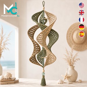 Könnte beinhalten: Ein hängendes Spiral-Mobile mit abwechselnden olivgrünen und beigen gehäkelten Paneelen in Gitteroptik. Die Struktur wird von einem zentralen Stab mit Holzperlen gehalten und endet in einer grünen Quaste mit einer einzelnen Perle.
