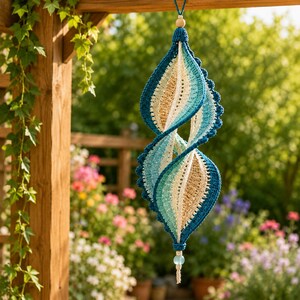 May include: A hanging spiral ornament crafted from crocheted yarn in shades of deep blue, turquoise, light blue, and beige. The structure features a twisted, elongated shape with a scalloped edge, suspended by a string with a wooden bead at the top.