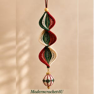 Peut inclure: Une décoration suspendue en crochet présentant un design en spirale multicolore avec du fil rouge, vert foncé et crème. La structure est surmontée d'une petite perle en bois et terminée par une sphère en crochet et des éléments dorés.