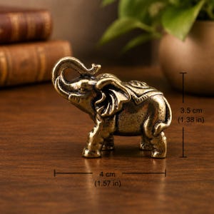 May include: A small brass elephant figurine with a metallic gold finish, featuring an upward-curved trunk and detailed ear textures. The figurine measures 4 inches in length and 3.5 inches in height as indicated by the visible measurement markers.