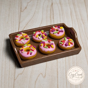 May include: A brown rectangular tray holding five miniature golden-brown donuts with pink icing and colorful sprinkles. The donuts are arranged in a cluster on the tray, which features small side handles and a smooth, glossy finish.