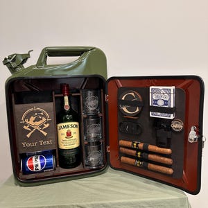 Könnte beinhalten: Ein olivgrüner Metallkanister, der zu einer Bar umgebaut wurde. Das Innere enthält einen Holzhalter mit Jagdmotiv und dem Text "Your Text", eine Flasche Jameson Whiskey, drei Gläser, Untersetzer, Spielkarten und Zigarren.