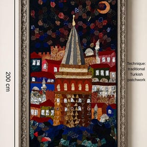 Può includere: Un'opera d'arte murale rettangolare con una raffigurazione in patchwork di una torre circondata da edifici sotto un cielo notturno con una luna crescente. L'opera misura 100 cm per 200 cm ed è in una cornice argentata. Testo: Technique: traditional Turkish patchwork.