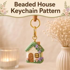 May include: A beaded house keychain featuring a white house with a brown door, a yellow window, and a green roof adorned with small pink and purple flowers. The house is attached to a gold-coloured metal keyring and lobster clasp hardware.