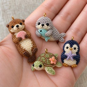 May include: Four small animal charms crafted from tiny beads. The set includes a brown otter holding a pink shell, a gray seal holding a light blue fish, a green sea turtle with a pink flower, and a dark blue penguin holding a purple starfish.