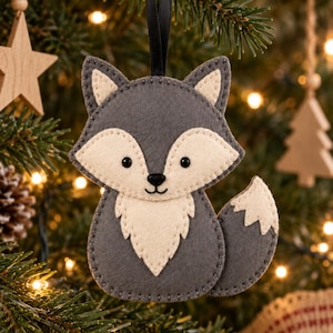 May include: A gray and cream felt fox ornament featuring stitched details, black bead eyes, and a small black nose. The fox has pointed ears, a fluffy chest patch, and a curved tail, suspended by a thin black ribbon for hanging on a tree.