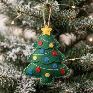 May include: A green felt Christmas tree ornament featuring a yellow star at the top, gold thread garland, and small circular red, blue, and yellow felt decorations stitched onto the surface, suspended by a thin brown twine loop.