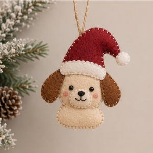 Könnte beinhalten: Ein Hunde-Anhänger aus Filz mit cremefarbenem Gesicht, braunen Ohren und einer roten Weihnachtsmütze mit weißem Bommel und Rand. Der Hund hat schwarze Perlenaugen, eine gestickte Nase und einen Mund sowie rosafarbene Wangen.