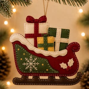 Puede incluir: Un adorno navideño de fieltro con forma de trineo rojo y verde que transporta tres cajas de regalo envueltas. El trineo presenta un bordado de copo de nieve blanco, un borde color crema y hojas de acebo. Cuelga de un cordel marrón fino.