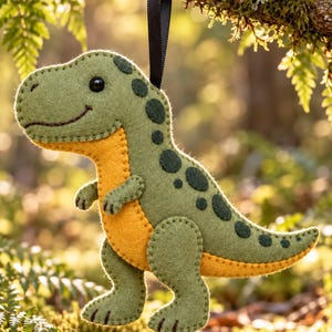 Puede incluir: Un adorno de fieltro con forma de dinosaurio que presenta un cuerpo verde claro con manchas verde oscuro y un vientre amarillo brillante. El dinosaurio tiene una boca cosida, un ojo de cuenta negra y una cinta negra para colgarlo.