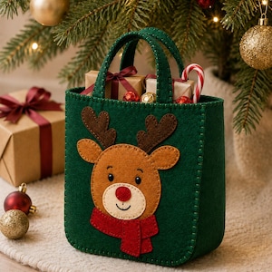May include: A dark green felt tote bag featuring a brown reindeer applique with dark brown antlers, a red nose, and a red scarf. The bag has two matching green felt handles and visible stitching along the edges, filled with small gift boxes and a candy cane.
