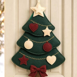 May include: A dark green felt Christmas tree wall hanging with a cream-coloured star at the top. The tree is decorated with stitched yellow garland lines and various felt ornaments, including cream and maroon hearts, stars, and circles, with a maroon bow.