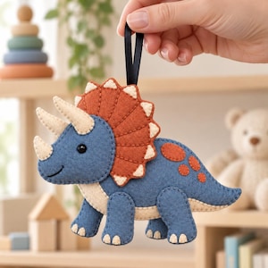 Peut inclure: Une décoration en feutrine en forme de tricératops avec un corps bleu, une collerette rouille à pointes crème et des cornes crème. Le dinosaure possède une boucle en ruban noir sur le dessus pour le suspendre et présente des coutures visibles.