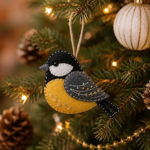 May include: A felt bird ornament featuring a black head, a white cheek patch, a yellow breast, and a dark gray wing with white and yellow embroidered details. The bird is suspended by a thin twine loop for hanging on a tree branch.