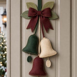 May include: A hanging felt decoration featuring three bells in dark green, cream, and burgundy. The bells are suspended from a central dark green strap topped with a burgundy felt bow and four light green felt leaves with stitched details.