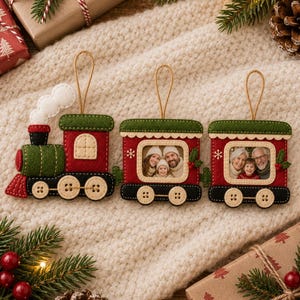 Könnte beinhalten: Ein dreiteiliges Zug-Ornament-Set aus Filz, bestehend aus einer Lokomotive und zwei Waggons. Jeder Waggon verfügt über einen rechteckigen Rahmen für ein Foto, verziert mit grünem, rotem und schwarzem Filz, weißen Nähten und Knopf-Rädern.