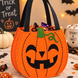 Peut inclure: Un sac à friandises en feutrine orange en forme de citrouille avec des anses noires, arborant un visage de jack-o'-lantern aux yeux, nez triangulaire et large sourire noirs. Il présente une tige verte et une vrille, avec des coutures noires.