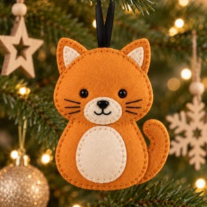 May include: A felt cat ornament in orange and cream with black embroidered whiskers, eyes, and a nose. The cat has pointed ears with cream accents, a round cream belly, and a curved tail. It hangs from a black ribbon loop for display.