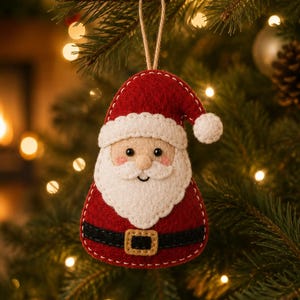 Puede incluir: Un adorno de fieltro con forma de Papá Noel que presenta un gorro rojo con pompón blanco, barba blanca y un cinturón negro con hebilla dorada. El adorno está confeccionado con costuras blancas visibles en los bordes y un lazo de yute.