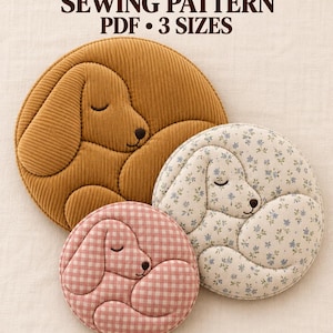 May include: A sewing pattern for a sleeping dog pillow in three sizes, 30, 40, and 50 cm. The image displays three circular pillows: one large solid mustard corduroy, one medium cream with blue floral print, and one small pink and white gingham.