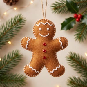 May include: A brown felt gingerbread person ornament featuring white embroidered stitching along the edges, white stitched wavy lines on the arms and legs, white X-shaped eyes, a white stitched smile, and three small red circular beads down the center.