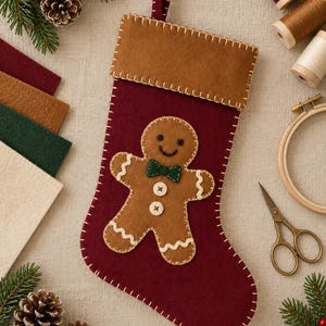 Könnte beinhalten: Ein dunkelroter Weihnachtsstrumpf aus Filz mit einer braunen Lebkuchenmann-Applikation, einer grünen Fliege und zwei weißen Knöpfen. Der Strumpf hat ein braunes Bündchen und weiße Zierstiche entlang der Kanten sowie eine kleine Schlaufe.