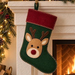 May include: A dark green felt Christmas stocking featuring a red cuff and a central reindeer applique. The reindeer has brown antlers, a tan face, black eyes, and a red nose. The entire stocking is finished with visible cream-coloured stitching.