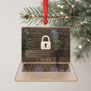 May include: A laptop-shaped ornament with a red ribbon hanger. The screen displays lines of computer code and a central padlock icon. Below the screen, a rectangular box contains the text 'Your Name' in a clear, sans-serif font.