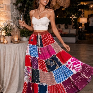 Puede incluir: Un top corto blanco sin mangas con corpiño fruncido combinado con una falda larga de patchwork de cintura alta. La falda presenta una mezcla vibrante de cuadrados de tela rojos, azules, morados y rosas con varios patrones florales y geométricos.