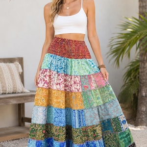 May include: A white sleeveless crop top paired with a floor-length tiered maxi skirt featuring a patchwork design of various colorful floral and paisley patterns in shades of red, green, blue, yellow, and black with an elasticized waistband.