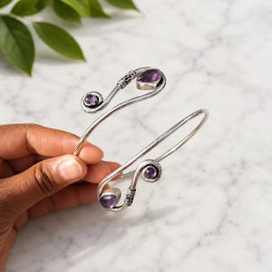 Peut inclure: Un bracelet manchette ouvert en métal argenté doté de deux extrémités en spirale. Chaque extrémité est ornée d'une petite pierre d'améthyste ronde violette et d'une pierre d'améthyste violette plus grande en forme de poire sertie.