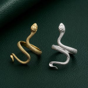 Op de afbeelding: Twee wikkelringen in de vorm van slangen, één in een goudkleurige tint en één in een zilverkleurige tint. Elke ring heeft een getextureerd, geschubd oppervlak dat slangenleer nabootst, met de kop van de slang boven op de ringband.