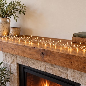 Op de afbeelding: Een flexibele lichtsnoer met talloze kleine, doorzichtige, druppelvormige lampjes bevestigd aan dunne, metalen draadtakken. De verlichte streng verspreidt een warme, gouden gloed en is horizontaal over een oppervlak geplaatst.
