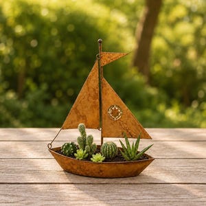 Peut inclure: Un pot de fleurs en forme de voilier en métal rouillé avec une voile triangulaire ornée d'une boussole découpée. La coque du bateau contient plusieurs petites plantes succulentes et cactus verts plantés dans du terreau sombre.