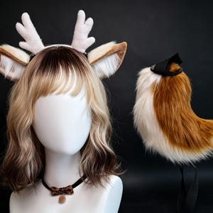Puede incluir: Un maniquí blanco con una diadema de astas de felpa blancas y orejas de piel sintética marrón y blanca, un collar tipo gargantilla con lazo de estampado de leopardo y una cola de piel sintética marrón y blanca con correa negra.