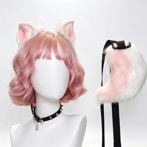 Può includere: Un set composto da una parrucca rosa ondulata con orecchie da gatto in pelliccia sintetica rosa chiaro e bianca, un collare nero borchiato con un ciondolo a forma di teschio argentato e una coda in pelliccia sintetica rosa e bianca.