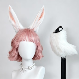 May include: A set featuring a pink wavy wig with long white rabbit ears, a white double-strap choker with silver buckles, and a fluffy white tail accessory with a black strap. The wig has bangs and shoulder-length hair styled in soft waves.