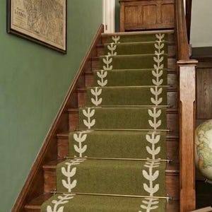 May include: A wooden staircase features a green carpet runner with a white leaf pattern, secured by brass stair rods. The walls are painted green, decorated with a framed map and a framed print of Big Ben. A wooden cabinet sits at the top landing.