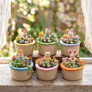 Könnte beinhalten: Sechs runde, gesprenkelte beige Keramik-Pflanzgefäße, jedes mit einem farbigen Rand und einer einzigartigen Miniatur-Tierfigur, umgeben von kleinen Sukkulenten. Die Ränder sind in Gelb, Grün, Hellblau, leuchtendem Blau, Rosa und Orange bemalt.