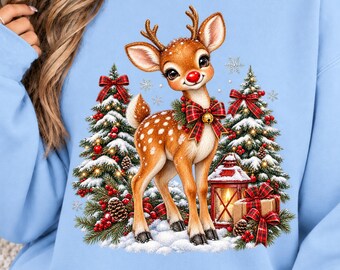 May include: A light blue sweatshirt featuring a graphic of a brown fawn with a red nose and a plaid bow around its neck. The fawn stands in snow between two snow-covered Christmas trees, a lit red lantern, and a gift box with a red plaid ribbon.
