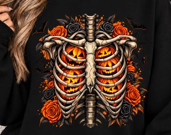 May include: A black sweatshirt featuring a graphic print of a human rib cage enclosing glowing orange jack-o'-lanterns. The design is surrounded by orange and black roses, small bats, and spiderwebs, creating a detailed seasonal illustration.