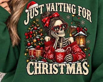 May include: A dark green sweatshirt featuring a graphic of a skeleton wearing heart-shaped sunglasses, a red bow, and a red sweater. The skeleton holds a mug of cocoa. Text reads "JUST WAITING FOR CHRISTMAS" with a tree, gifts, and a lantern.