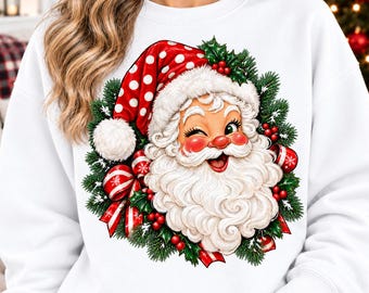 May include: A white long-sleeve sweatshirt featuring a graphic of a winking Santa Claus wearing a red hat with white polka dots. The Santa illustration is surrounded by a wreath of green pine needles, red berries, and red and white striped ribbons.