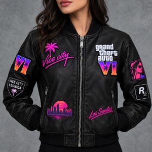 Könnte beinhalten: Eine schwarze Bomberjacke mit verschiedenen bunten Aufnähern, darunter die Schriftzüge Grand Theft Auto VI, Vice City und Los Santos. Die Jacke verfügt über einen Frontreißverschluss, gerippte Bündchen und neonfarbene Grafikdesigns.