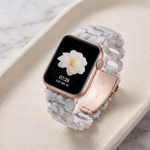 May include: A smartwatch with a rose gold metal case and a white and gray marbled resin link band. The digital display shows a white flower graphic, the time 07:26, and the date TUE SEP 10. The band features a rose gold stainless steel clasp.