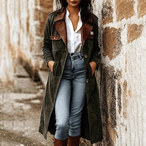 May include: A long olive green coat with brown leather lapels and pocket flaps, worn over a crisp white button-down shirt and light blue denim jeans. The coat features a front button closure and a structured collar, creating a layered look.