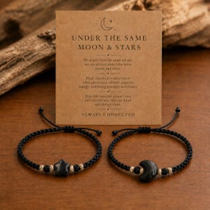 Puede incluir: Dos pulseras de cordón negro con pequeñas cuentas y un dije central. Una pulsera tiene un dije negro en forma de estrella y la otra un dije negro en forma de media luna. Se presentan con una tarjeta titulada UNDER THE SAME MOON & STARS.