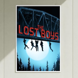 May include: A movie poster for The Lost Boys featuring a dark metal bridge structure with the red text THE LOST BOYS. Five silhouettes of people hang from the bridge against a large, bright white full moon and a dark blue forest silhouette.
