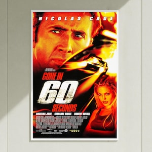 May include: A movie poster for Gone in 60 Seconds featuring a large close-up of Nicolas Cage at the top and Angelina Jolie at the bottom right. The title Gone in 60 Seconds is printed in large white letters over a dark background with orange highlights.